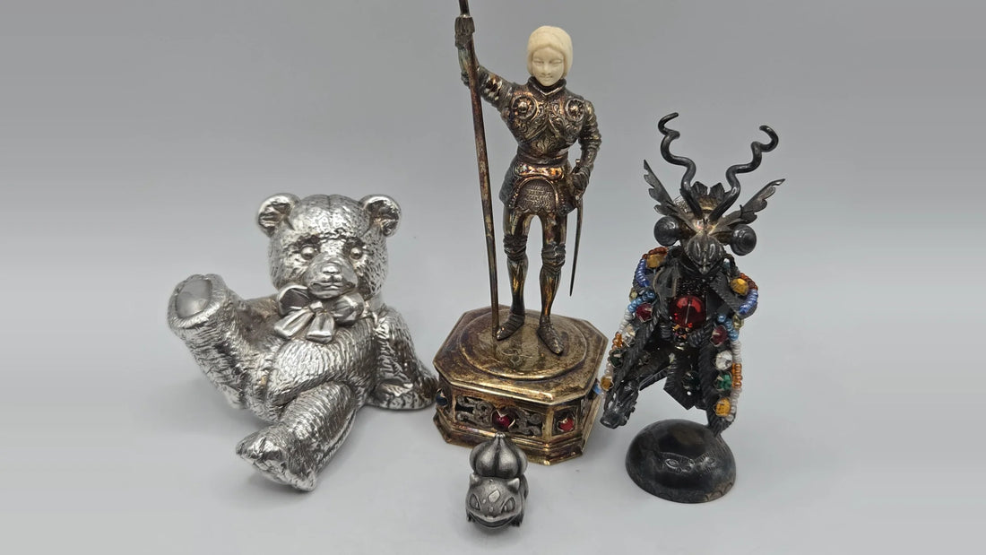 Five silver figurines from the Better Than Bullion collection showing different surface states — a mirror-bright teddy bear, an iridescently toned armoured knight on a gilt base, a black-patinated jewelled figure, and a matte grey character figurine